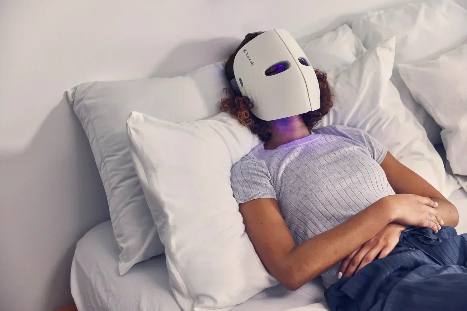 Person lying on bed wearing a theraface led mask for skincare treatment and relaxation