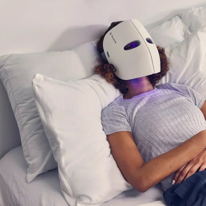 Person lying on bed wearing a theraface led mask for skincare treatment and relaxation