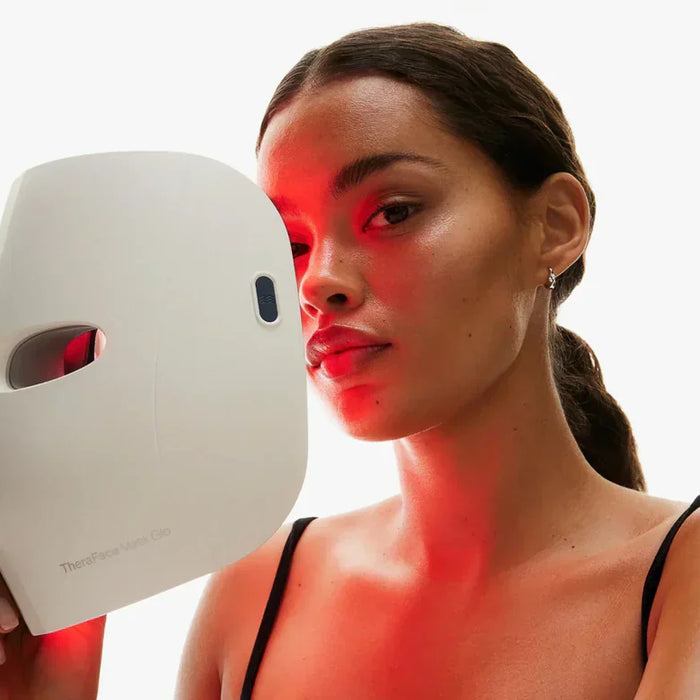 Woman using a theraface mask glo skincare device emitting red light on her face