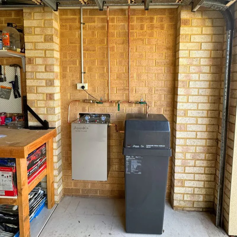 AquaCo water softening filter system installed in a garage with brick walls and pipes