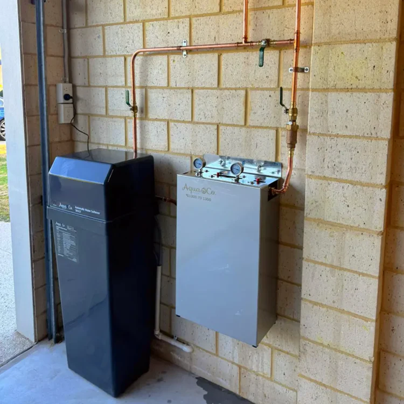 AquaCo water softening filter system installed on a wall with copper piping in a utility area
