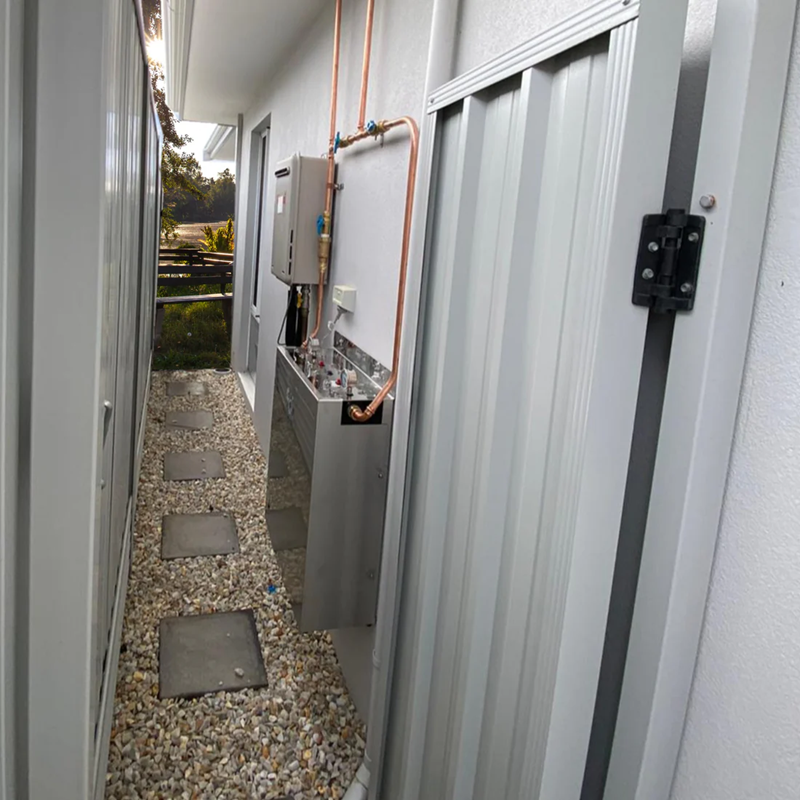 AquaCo whole house water filter installation with copper piping on an outdoor narrow pathway