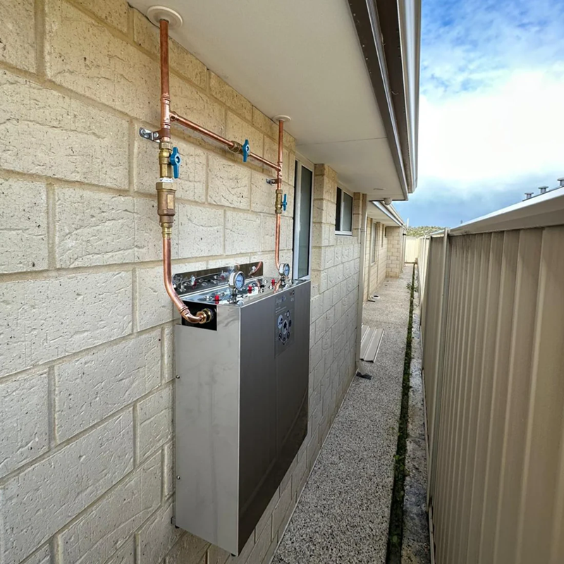 AquaCo whole house water filter installed on exterior wall with copper pipe connections