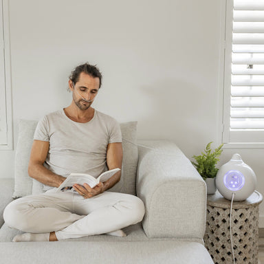 Man sitting on sofa reading book using hydrogen breathing system from HYDROGEN HEALTH beside him
