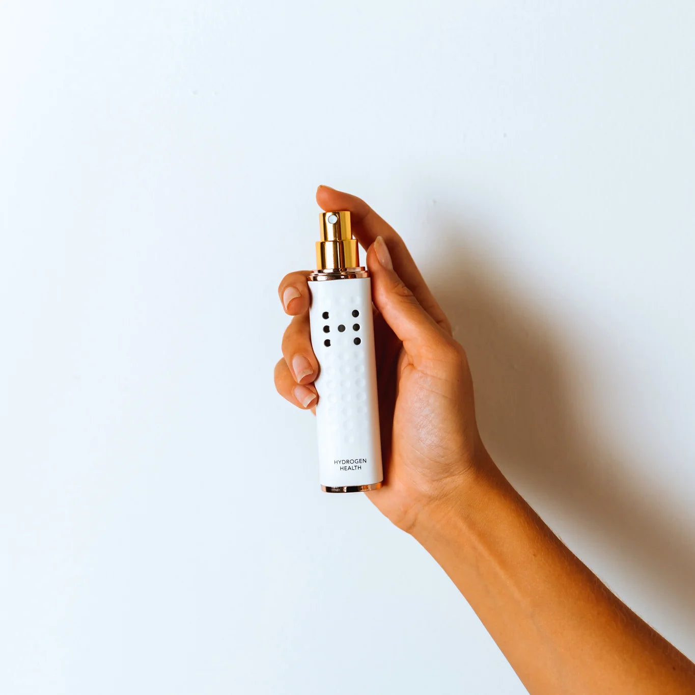 Hand holding HYDROGEN HEALTH hydrogen skin mister in white with gold spray nozzle for personal care