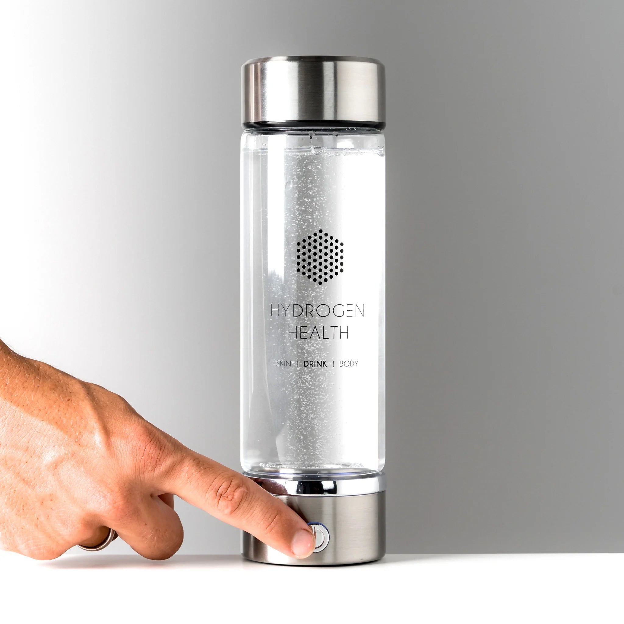 HYDROGEN HEALTH hydrogen water bottle with stainless steel cap and base being activated by a hand