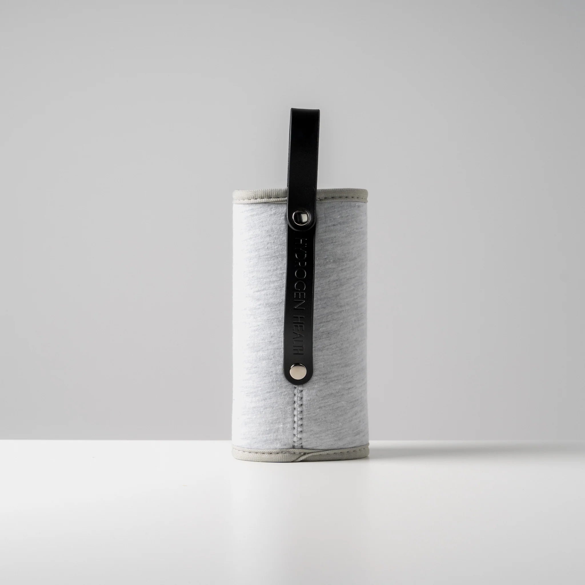 HYDROGEN HEALTH hydrogen water bottle cover in light gray with black strap standing on white surface