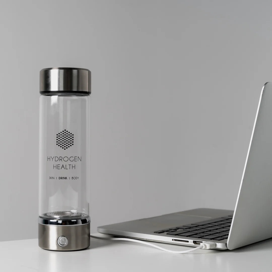 Hydrogen Health hydrogen water bottle with stainless steel lid next to a silver laptop on a white desk