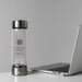 Hydrogen Health hydrogen water bottle with stainless steel lid next to a silver laptop on a white desk