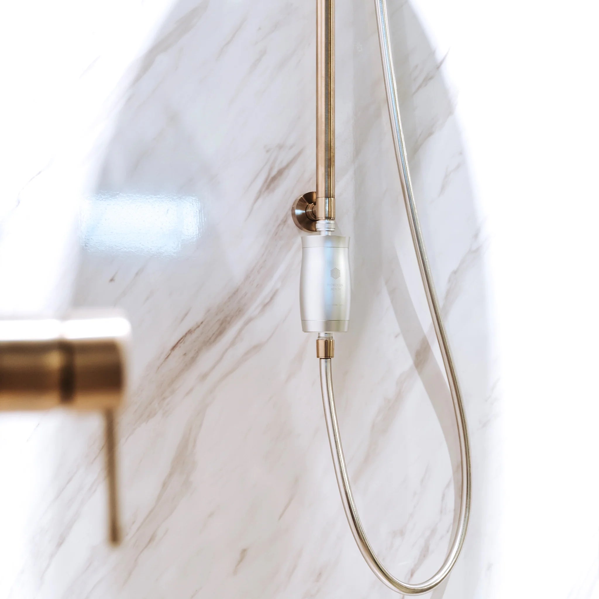 Hydrogen Health shower filter attached to a gold handheld showerhead on marble bathroom wall