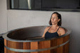 Woman relaxing in a wooden Stryke Recovery ice bath for muscle recovery and cold therapy
