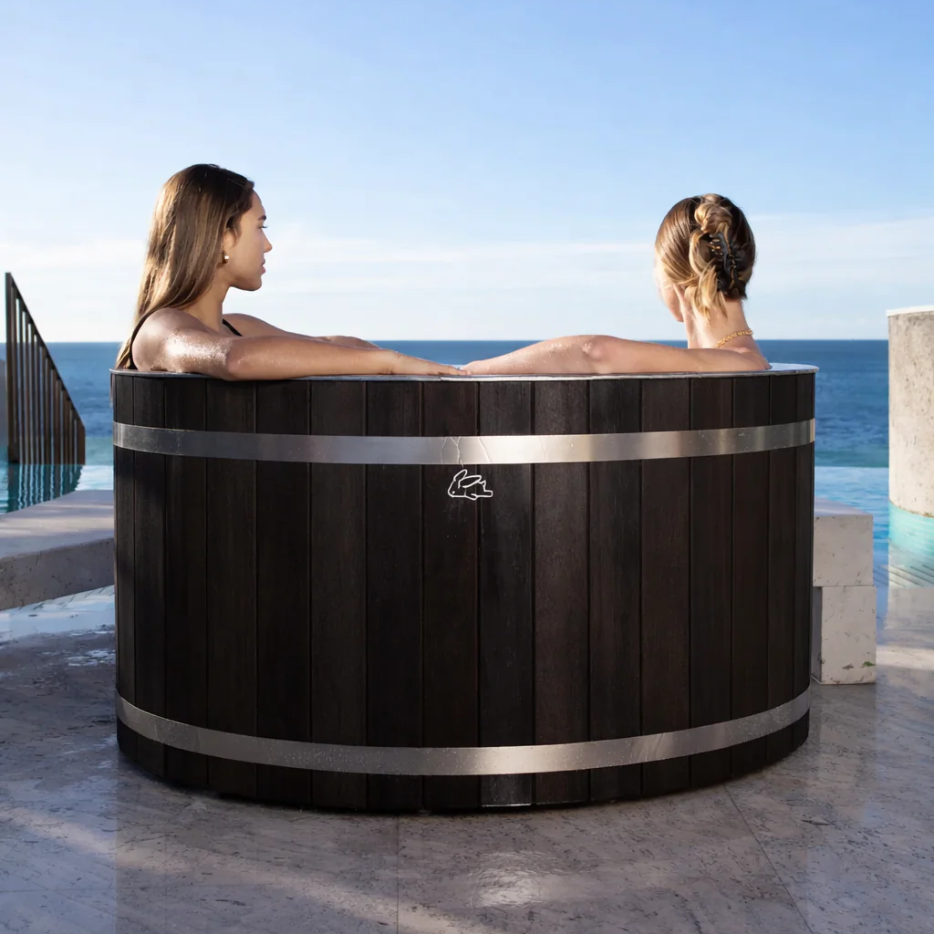 Chill Bunny dark wooden ice bath with two women relaxing outdoors by the ocean