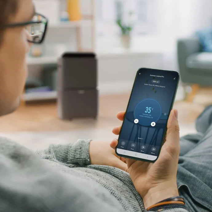 Person using smartphone app to control Ionmax dehumidifier in a cozy living room