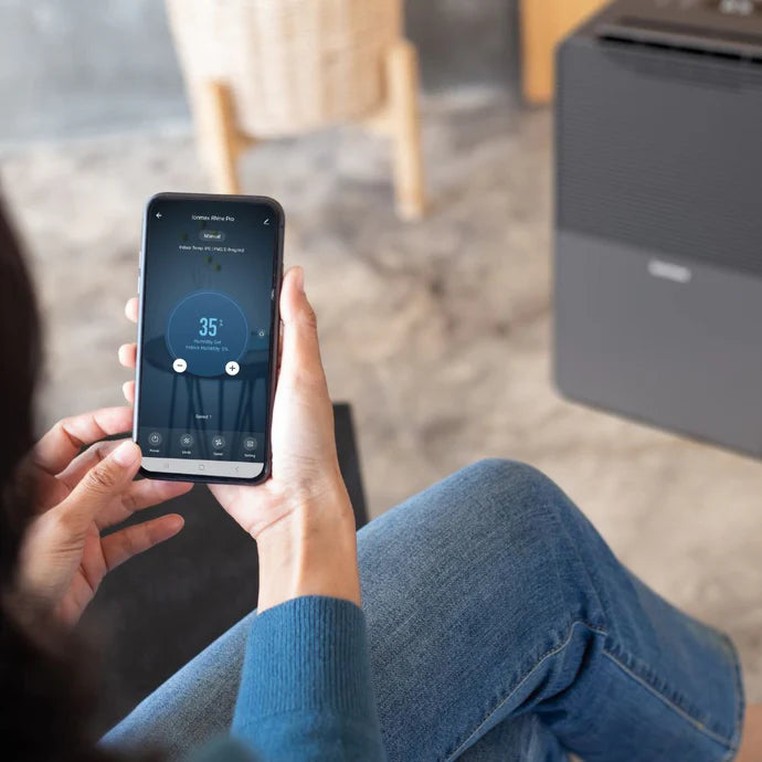 Person controlling Ionmax dehumidifier remotely using smartphone app in a modern living room
