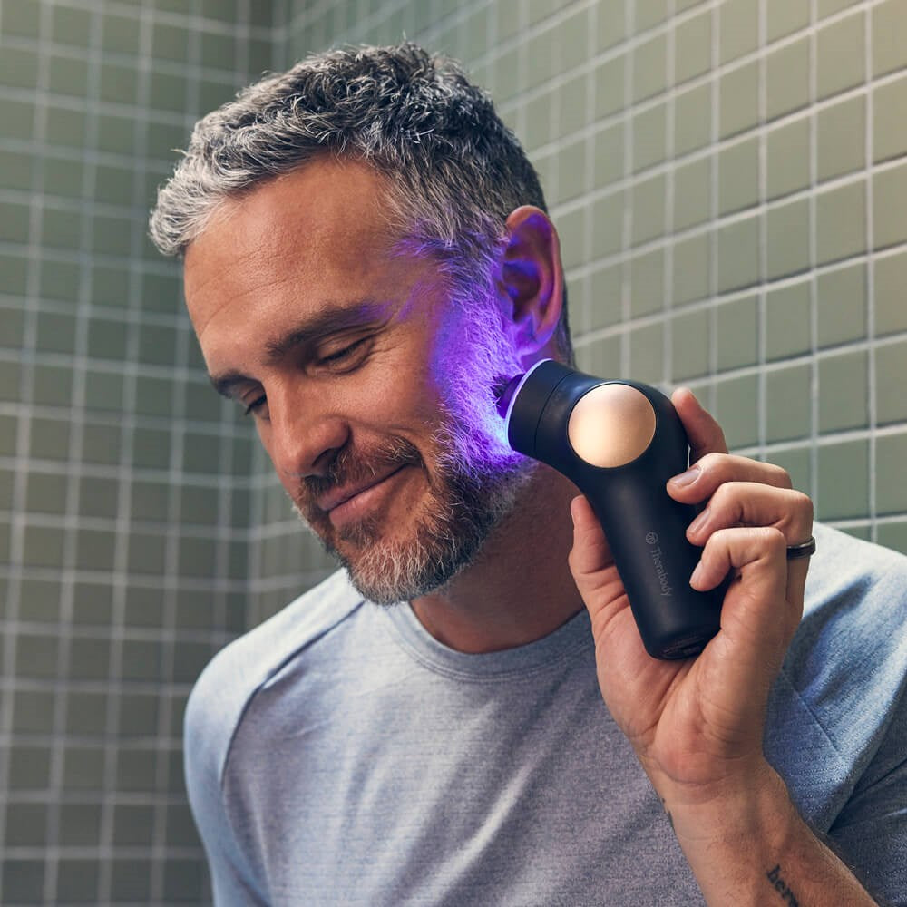 Man using Therabody theraface pro skincare device with glowing blue light on face