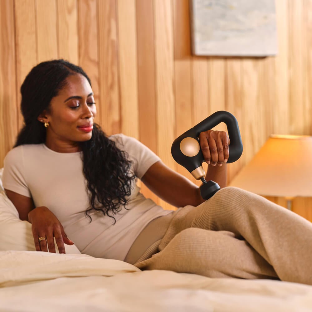 Therabody massage gun in black used by woman relaxing on bed for muscle relief