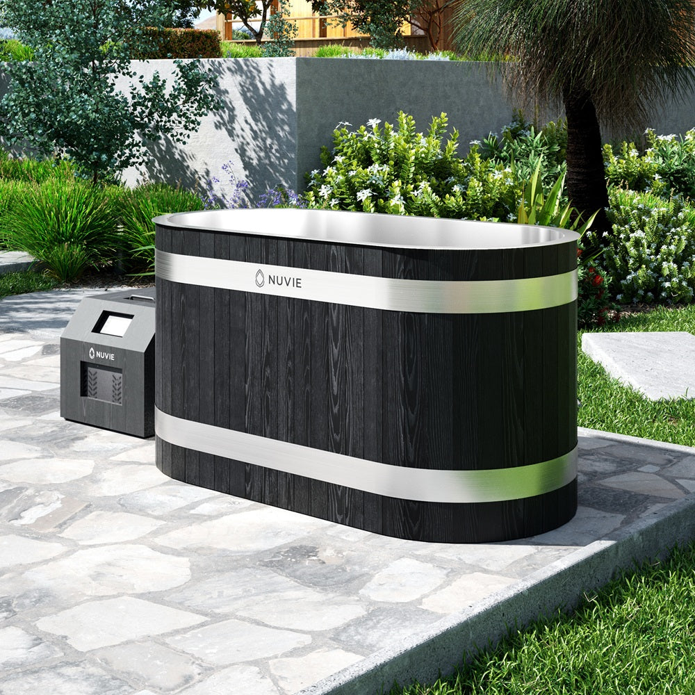 Nuvie black wood finish outdoor ice bath with stainless steel bands on a stone patio surrounded by greenery