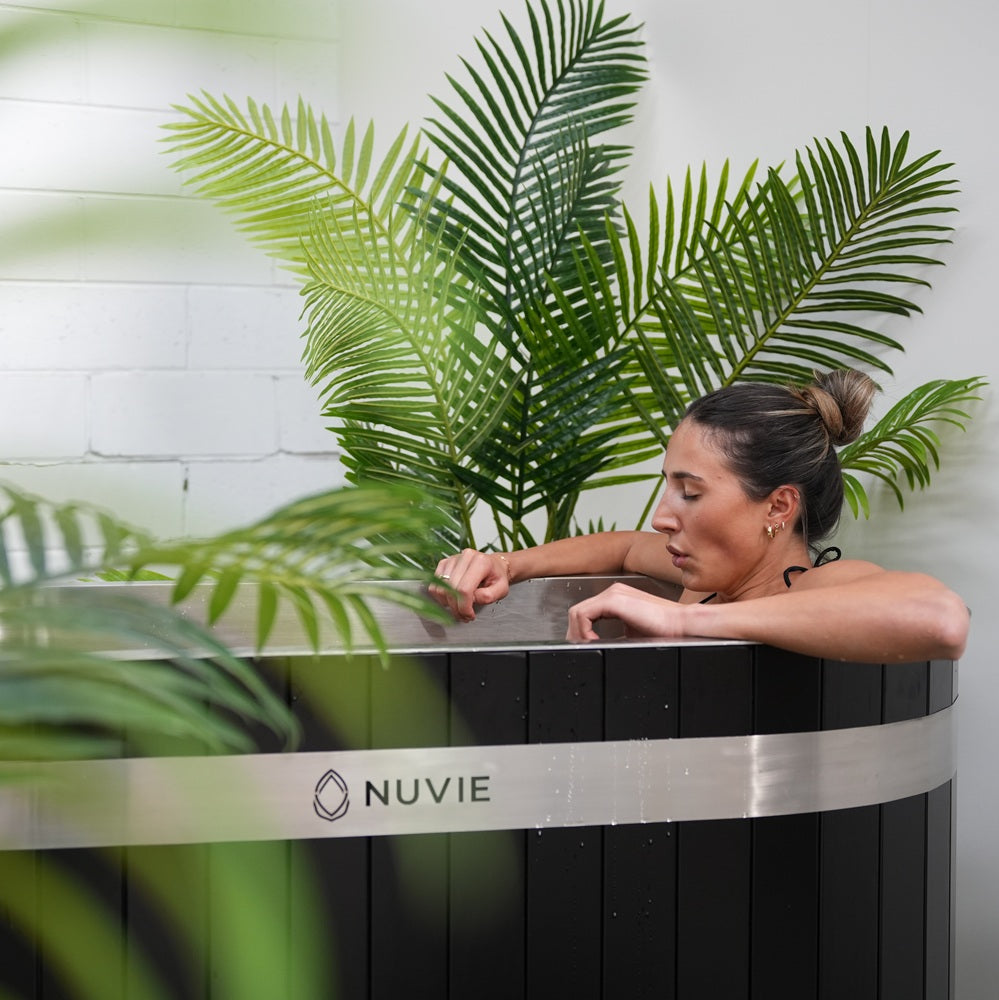 Woman relaxing in a Nuvie ice bath surrounded by green plants in a modern indoor setting
