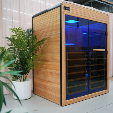 Nuvie infrared sauna with wooden exterior and blue glass door next to green potted plants indoors