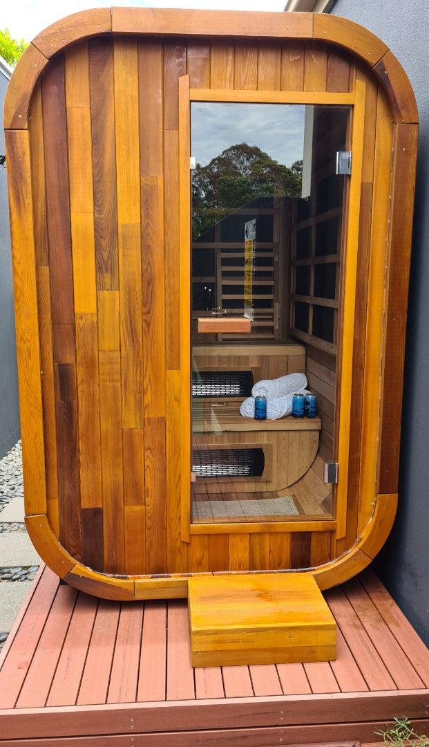 Stryke Recovery outdoor infrared sauna made of wood with glass door, towels, and seating inside