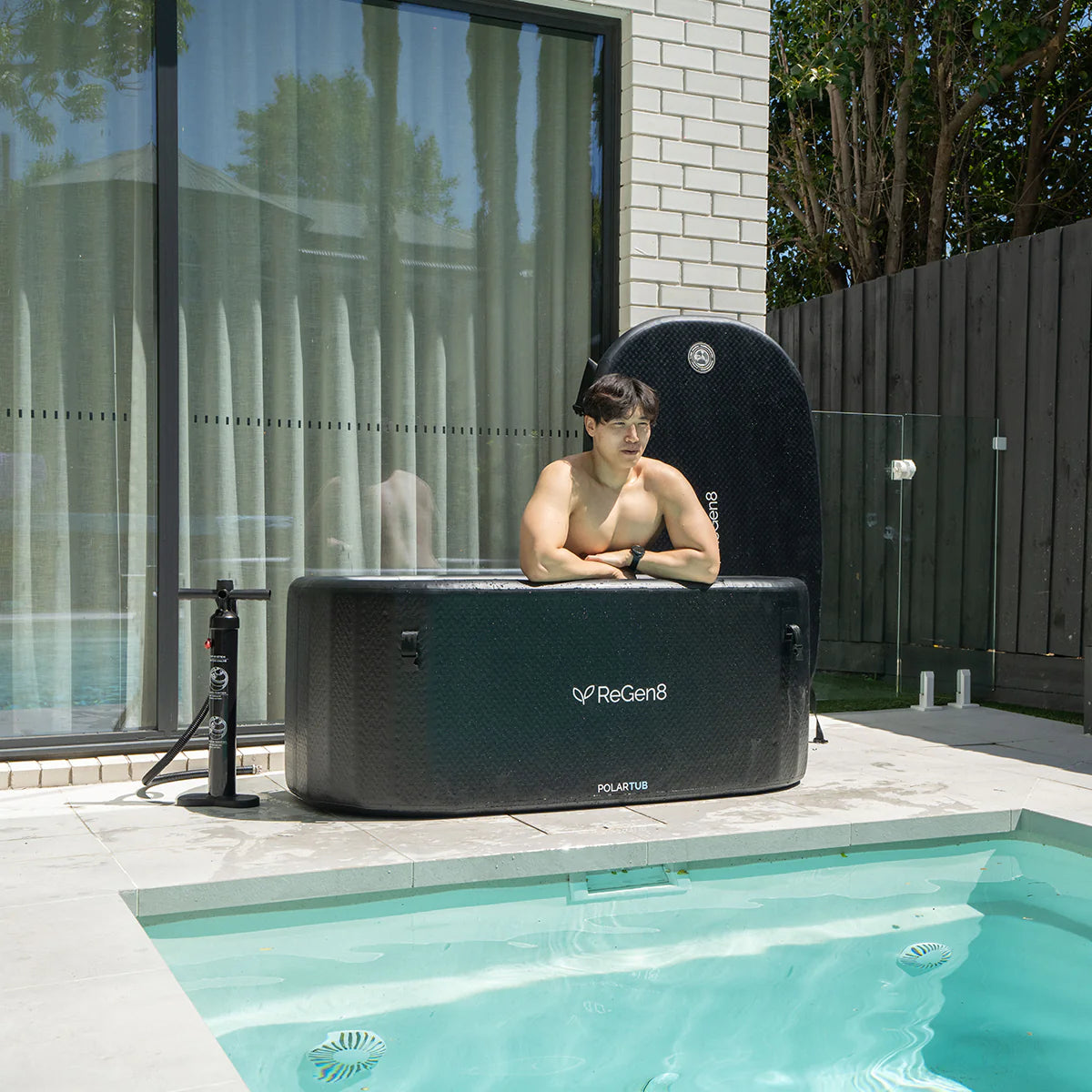 Lifespan Fitness black ReGen8 ice bath with man relaxing outdoors beside a swimming pool