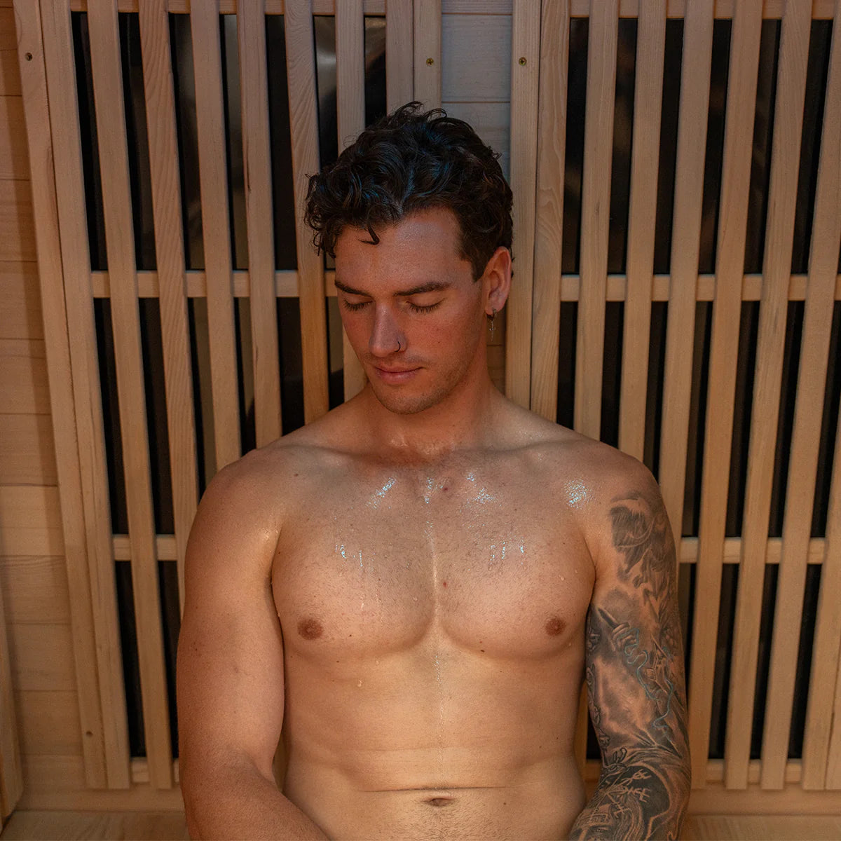 Man relaxing inside a Lifespan Fitness sauna with wooden slat walls and visible sweat on chest