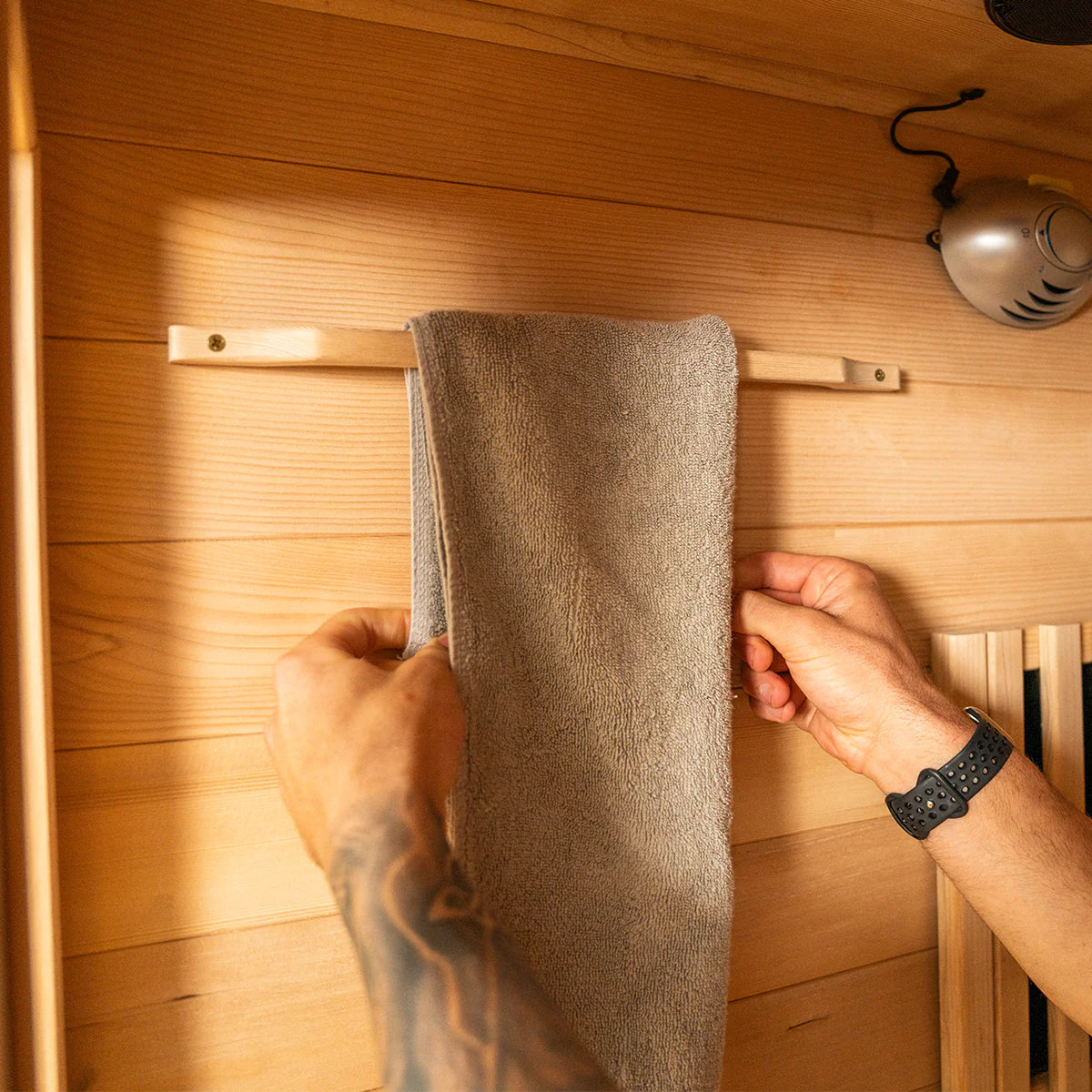Hands hanging a gray towel inside a Lifespan Fitness wooden sauna with warm lighting
