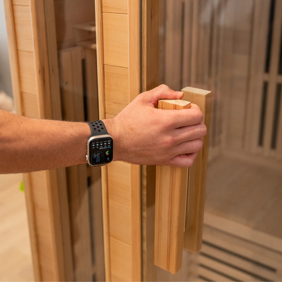 Person opening Lifespan Fitness wooden sauna door with glass panel and wooden handle