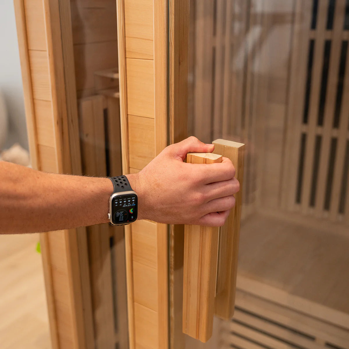 Person opening Lifespan Fitness wooden sauna door with glass panel and wooden handle