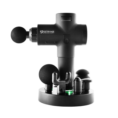 Stryke Recovery massage gun in black with multiple interchangeable heads on a round charging stand