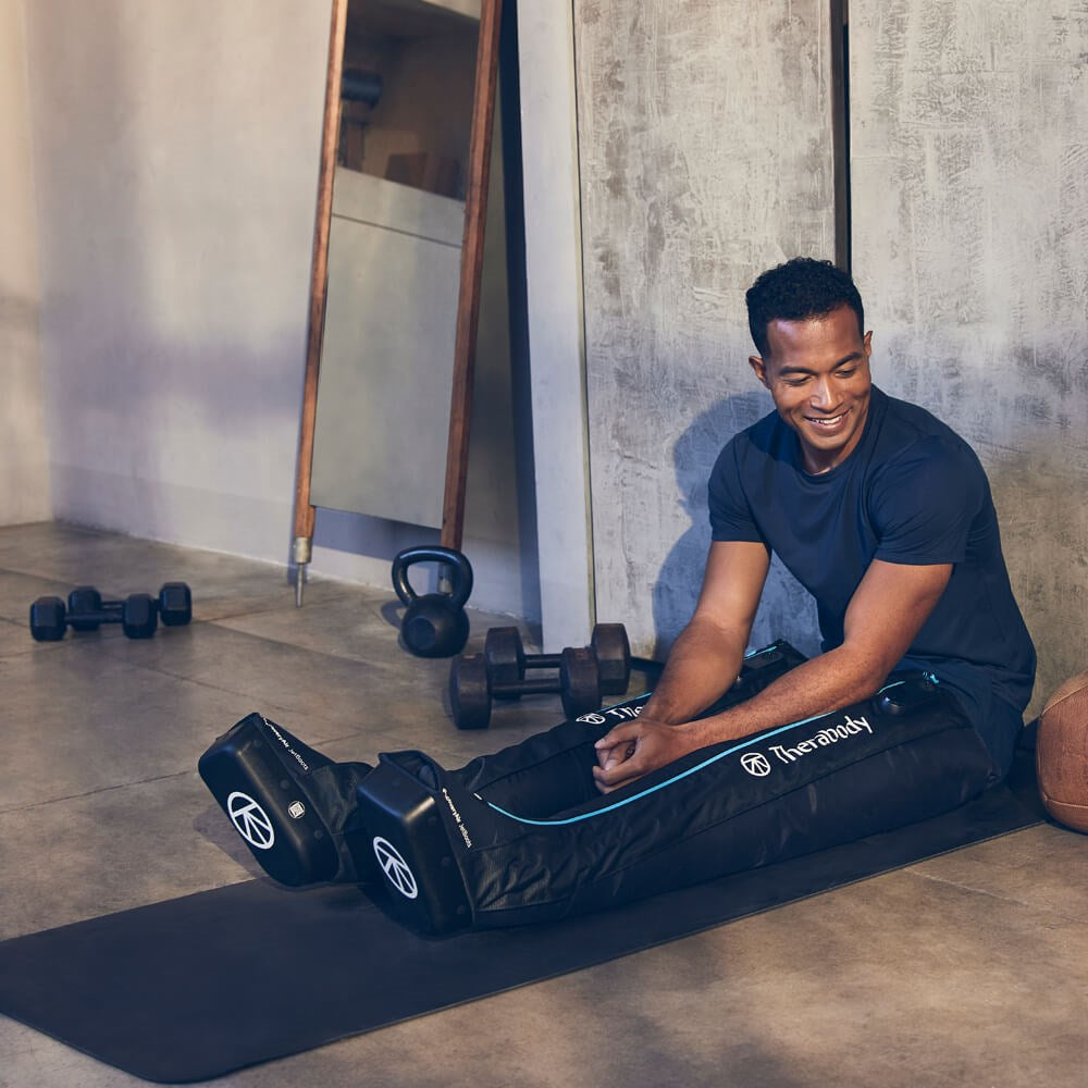 Therabody compression boots worn by man sitting on yoga mat for muscle recovery and improved circulation