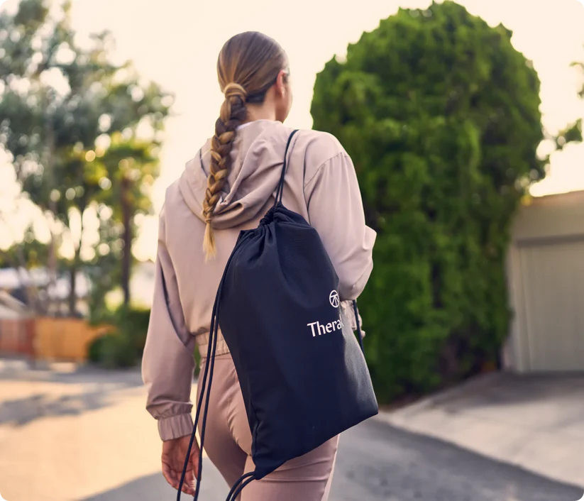 Woman carrying Therabody compression boots black carrying bag outdoors in casual outfit