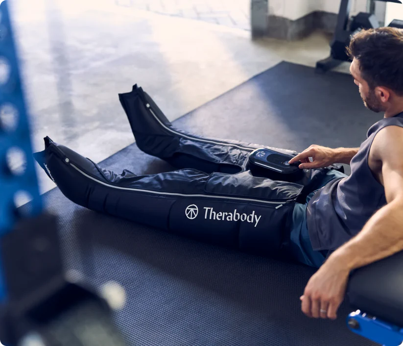 Therabody compression boots worn by man using control device for leg recovery and muscle relief