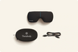 Therabody eye and temple massager with carrying case and charging cable on beige background