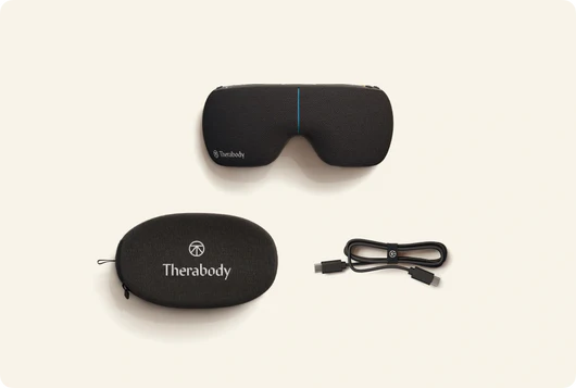 Therabody eye and temple massager with carrying case and charging cable on beige background