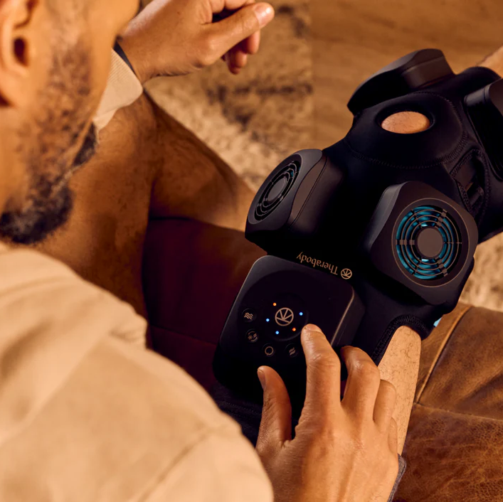 Therabody recoverytherm knee hot and cold therapy device being used on a man's knee for pain relief