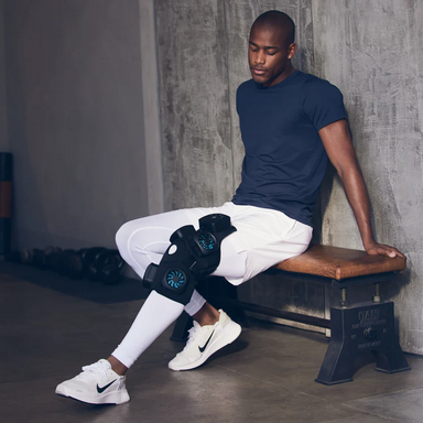 Therabody recoverytherm knee hot and cold therapy device worn on knee of man sitting on bench
