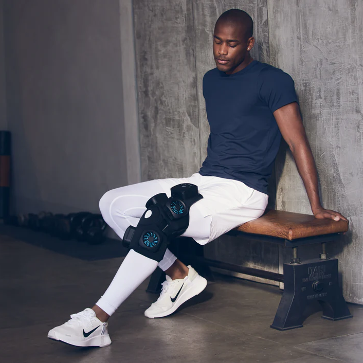 Therabody recoverytherm knee hot and cold therapy device worn on knee of man sitting on bench