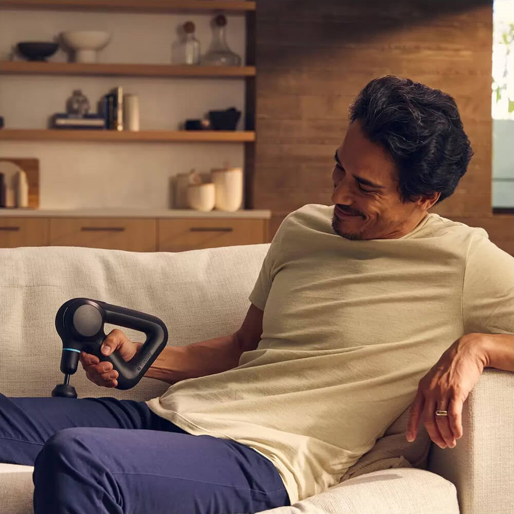 man using therabody theragun prime g5 on the couch