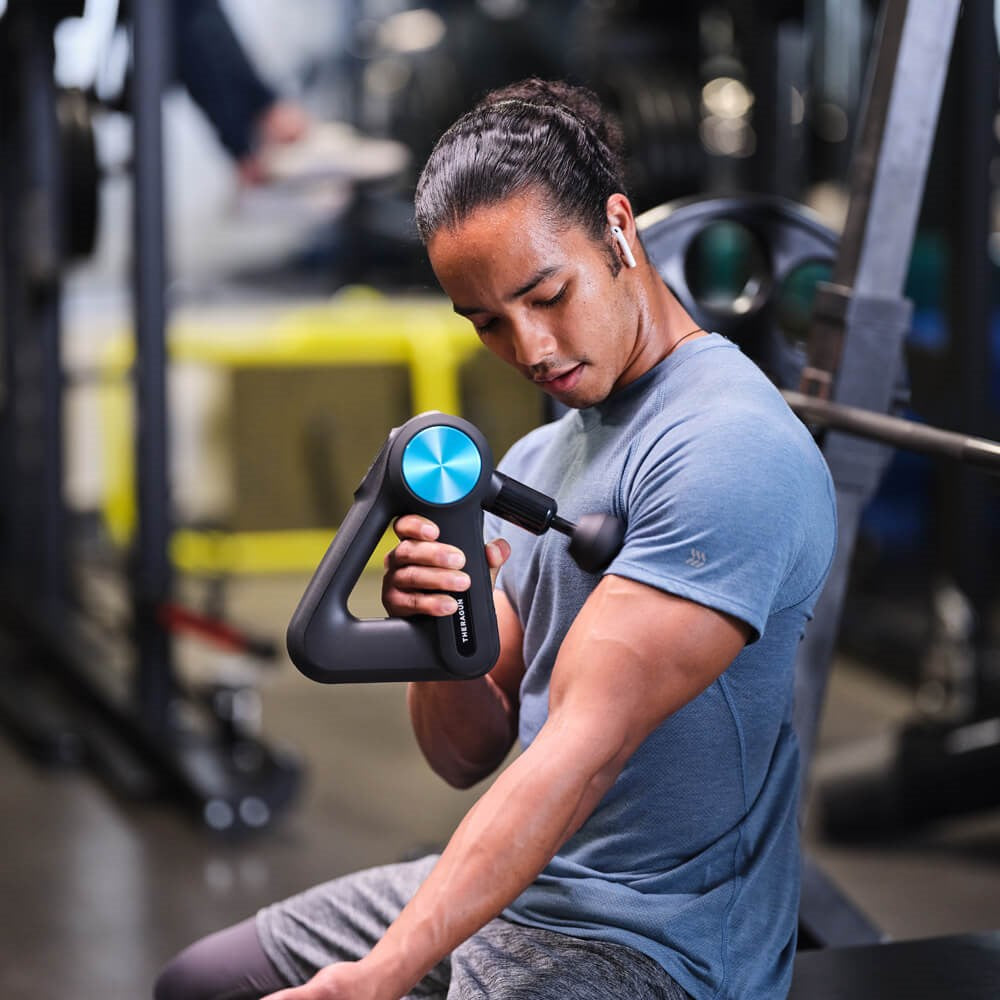 Therabody massage gun being used by man in gym for muscle relief and recovery