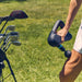 Therabody massage gun being used on leg muscles outdoors near a golf bag with clubs