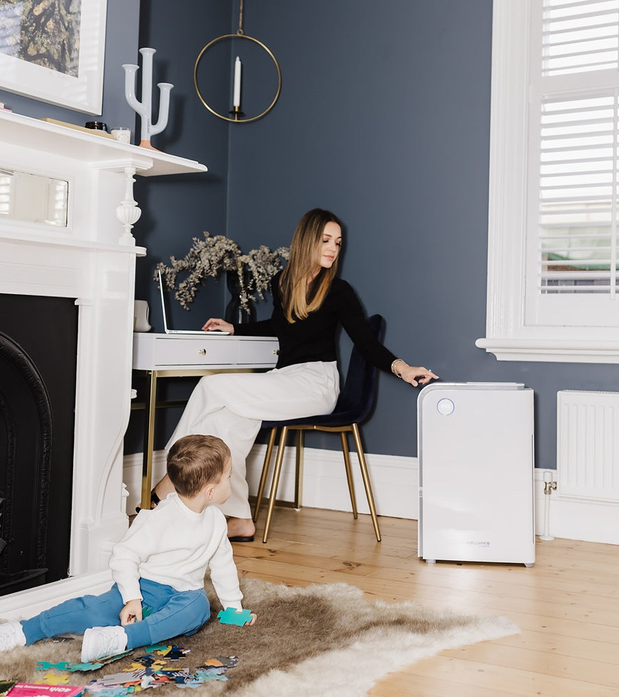 Welcare air purifier in white placed next to a woman sitting on chair and child playing on rug in modern living room