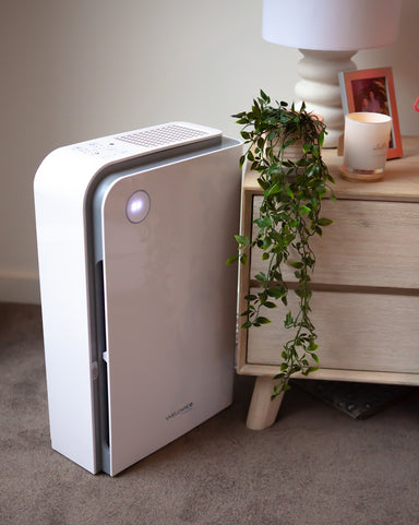 Welcare air purifier with sleek white design placed on carpet next to wooden nightstand with lamp and plant