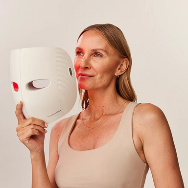 Therabody LED face mask held by woman with red light therapy on her cheek for skin treatment