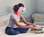 Therabody LED face mask worn by woman sitting on bed folding laundry in cozy bedroom