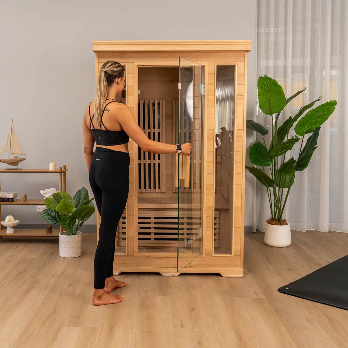 Woman opening glass door of Lifespan Fitness wooden sauna in a modern living room setting